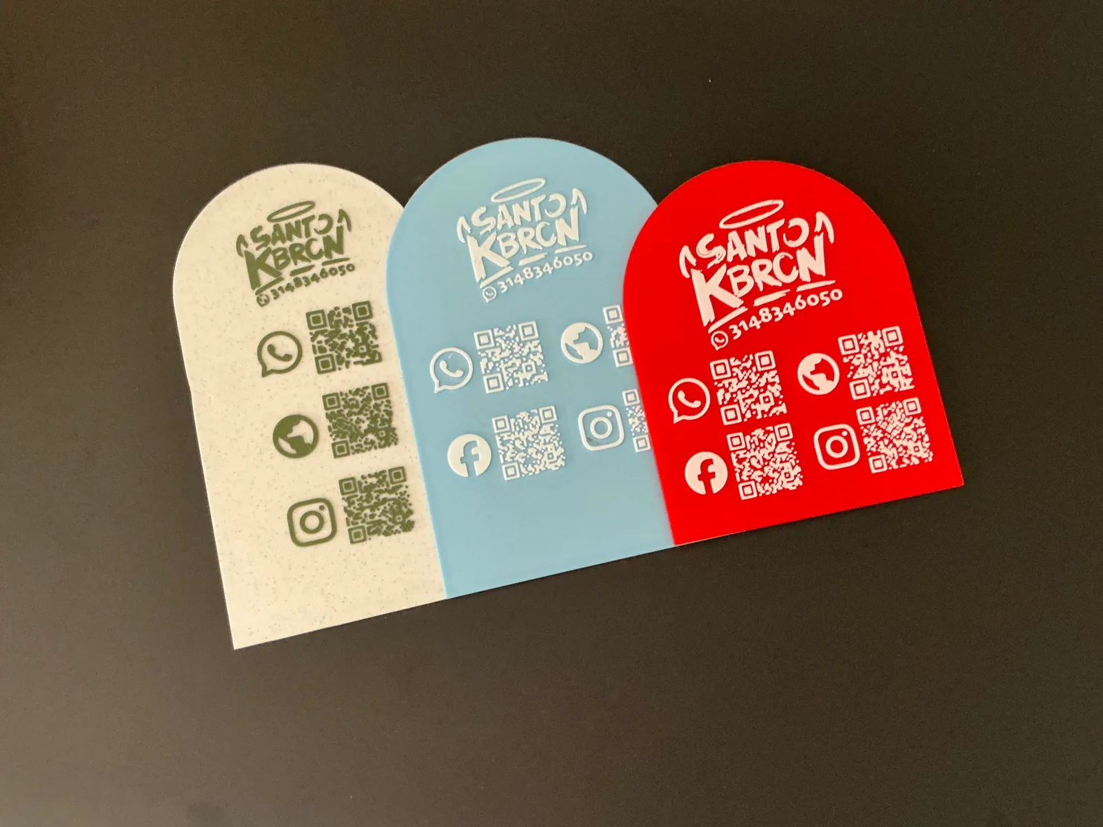Tres Placas Portátiles QR en crema, azul claro y roja puestas una al lado de la otra sobre fondo negro, cada una con el logo del negocio y sus códigos QR — Placa Portátil QR de Solid Lab 3D, Colombia