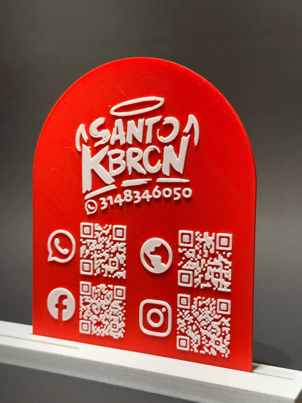 Placa QR con base roja en ángulo sobre su base blanca, con el logo del negocio en relieve blanco y cuatro códigos QR de redes sociales — Solid Lab 3D, Colombia
