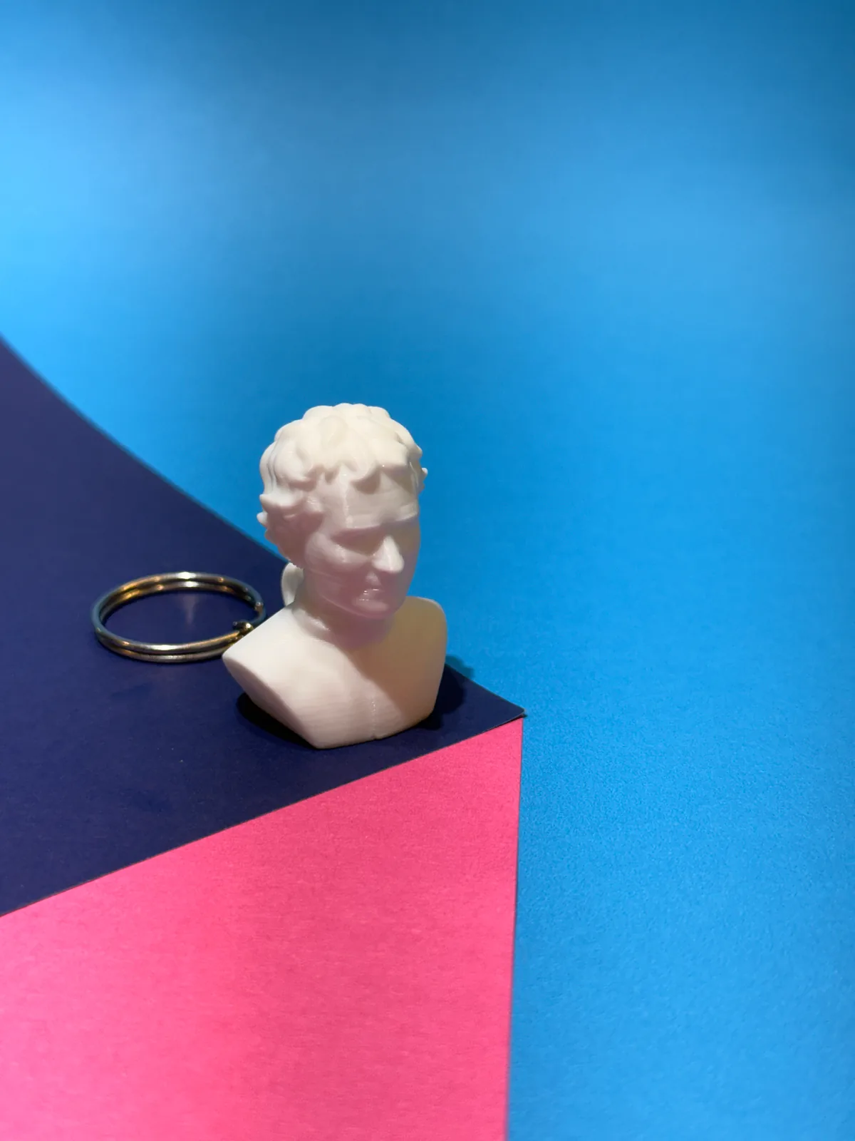 Llavero temático con forma de busto en blanco con la argolla al lado, tomado de frente sobre el mismo montaje de cartulinas de colores — Llaveros e imanes de Solid Lab 3D, Colombia