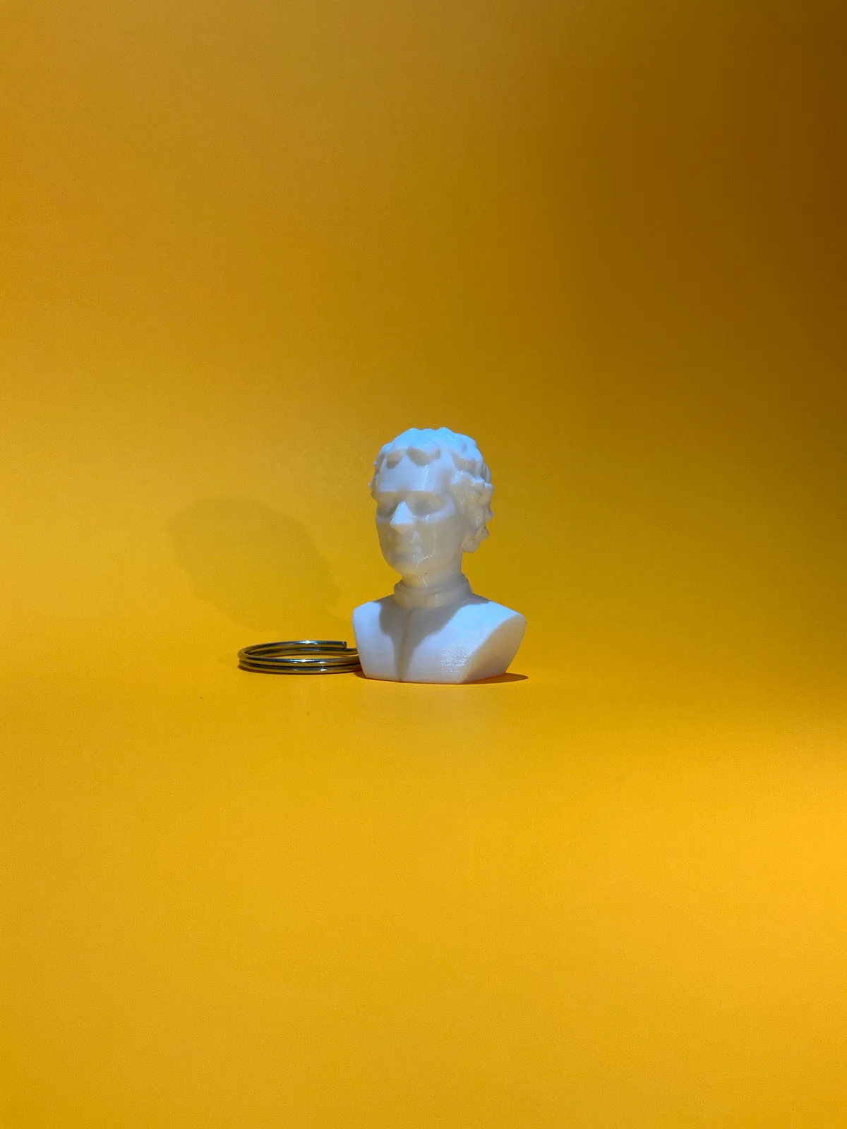 Llavero temático con forma de busto en blanco de frente y en primer plano sobre fondo amarillo, con la argolla metálica apoyada detrás — Llaveros e imanes de Solid Lab 3D, Colombia