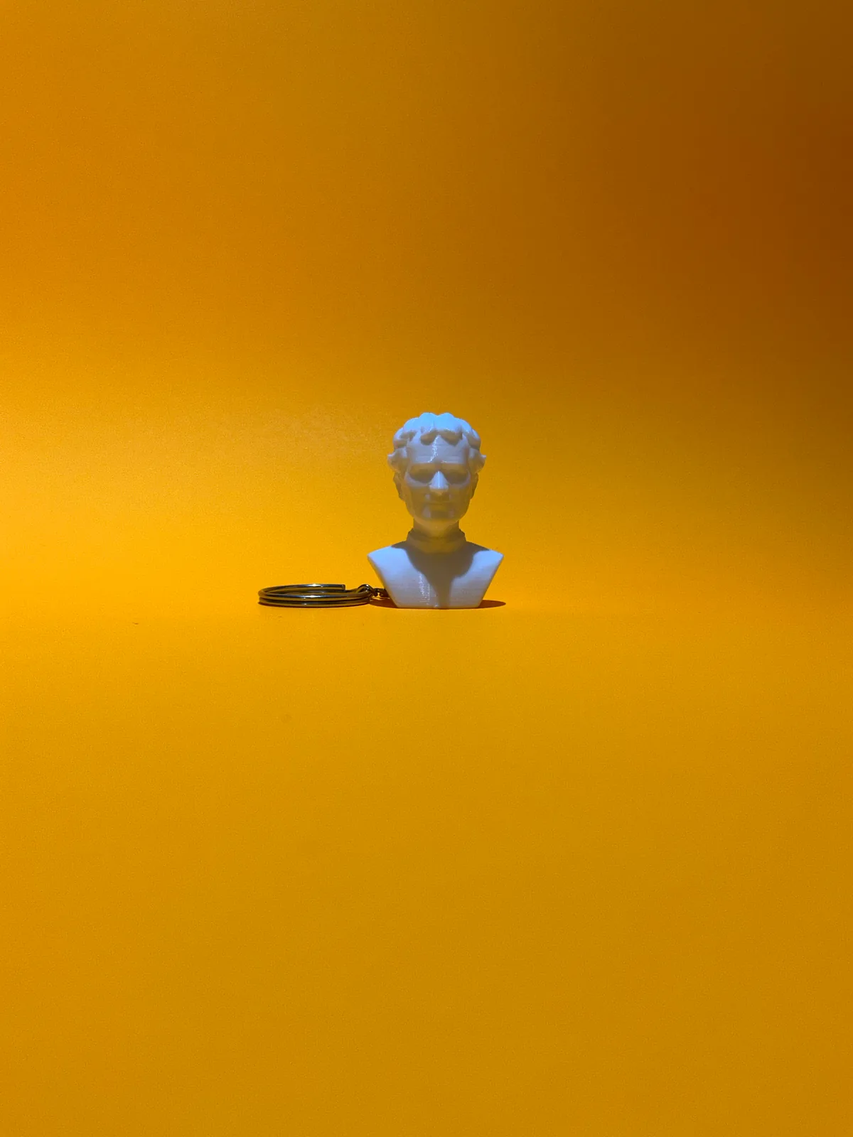 Llavero temático con forma de busto en blanco visto en plano abierto sobre fondo amarillo, para hacerse una idea del tamaño real de la pieza — Llaveros e imanes de Solid Lab 3D, Colombia