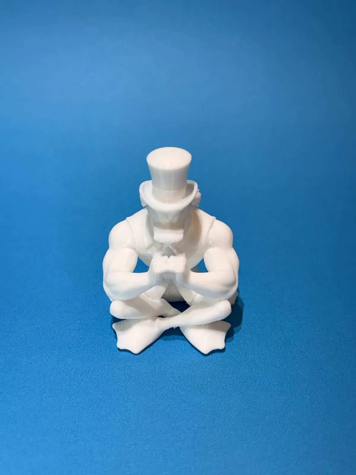 Figura temática de un personaje sentado con sombrero de copa impresa en blanco y tomada de frente sobre fondo azul, con los detalles de la cara y las manos definidos — Llaveros e imanes de Solid Lab 3D, Colombia