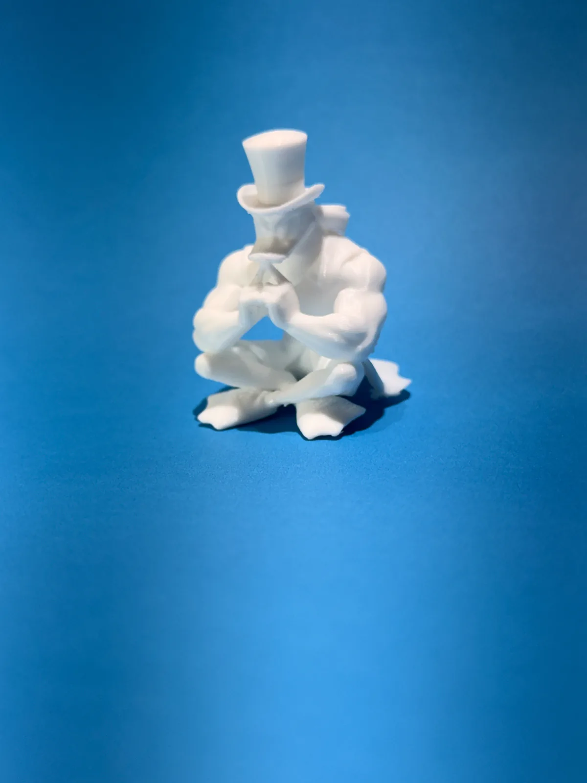 Figura temática de un personaje sentado con sombrero de copa en blanco sobre fondo azul, tomada desde arriba y de lado para ver cómo quedan las piernas cruzadas — Llaveros e imanes de Solid Lab 3D, Colombia