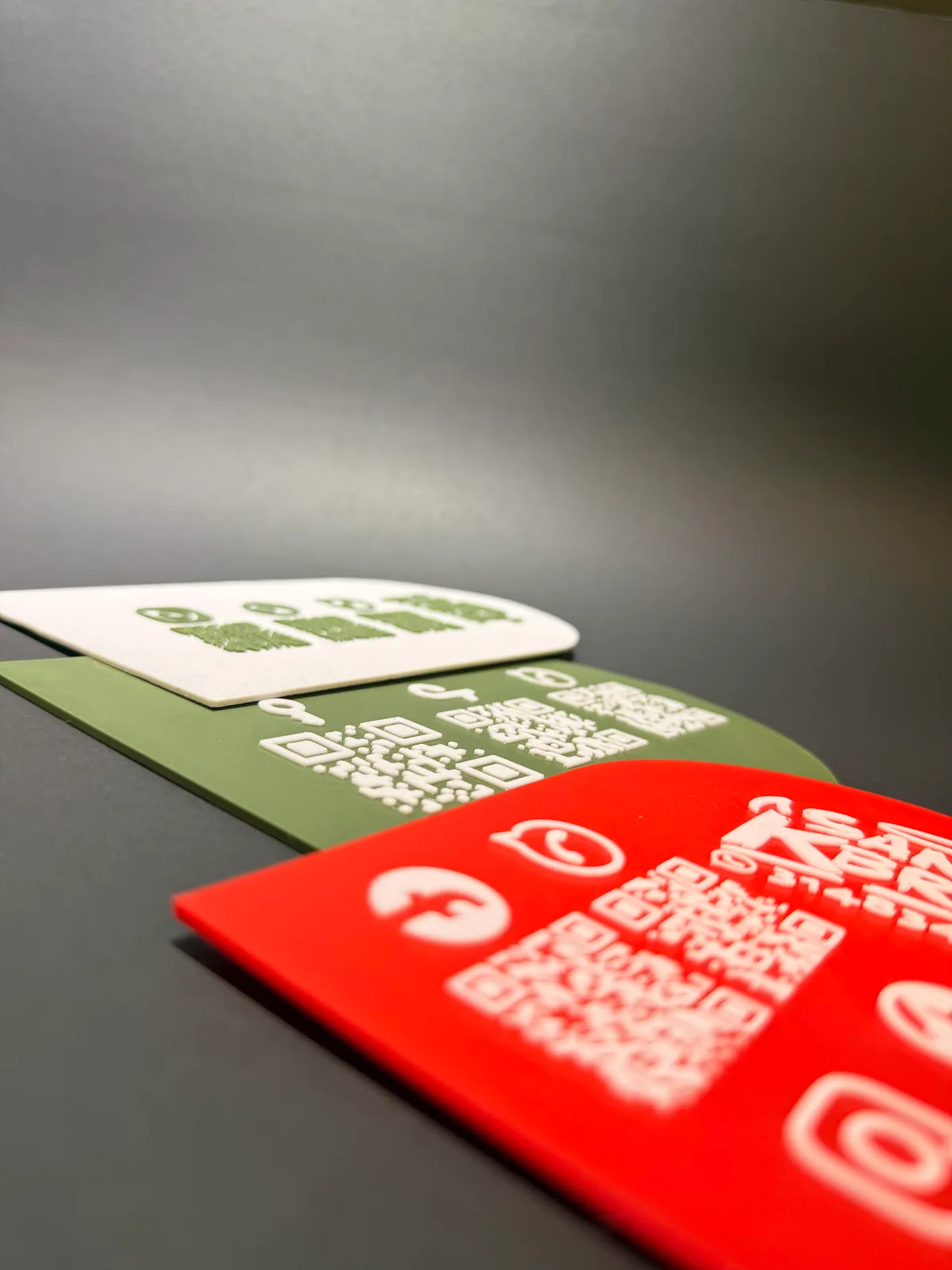 Placa Portátil QR vista casi a ras de la mesa junto a otras dos, en una toma que deja ver lo delgada y lo plana que es la pieza — Solid Lab 3D, Colombia