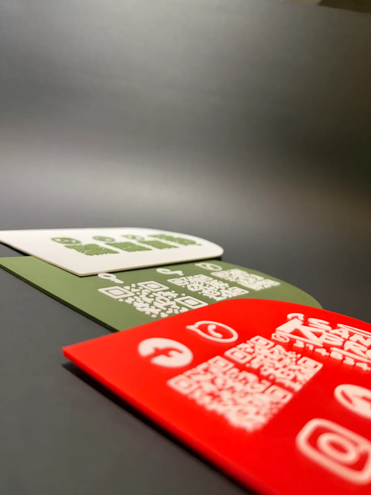 Tres Placas Portátiles QR en una toma rasante y cerrada con la roja en primer plano desenfocada, donde se nota el espesor real de la lámina impresa — Placa Portátil QR de Solid Lab 3D, Colombia