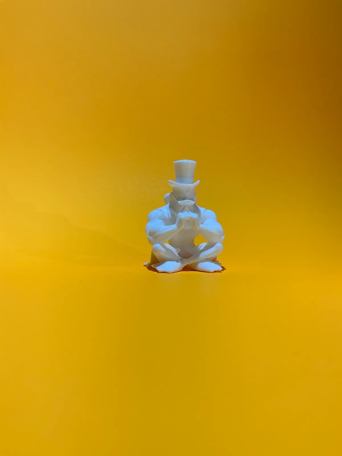 Figura temática de un personaje sentado con sombrero de copa en blanco sobre fondo amarillo, un ejemplo de pieza hecha con la forma de lo que vende el negocio — Llaveros e imanes de Solid Lab 3D, Colombia